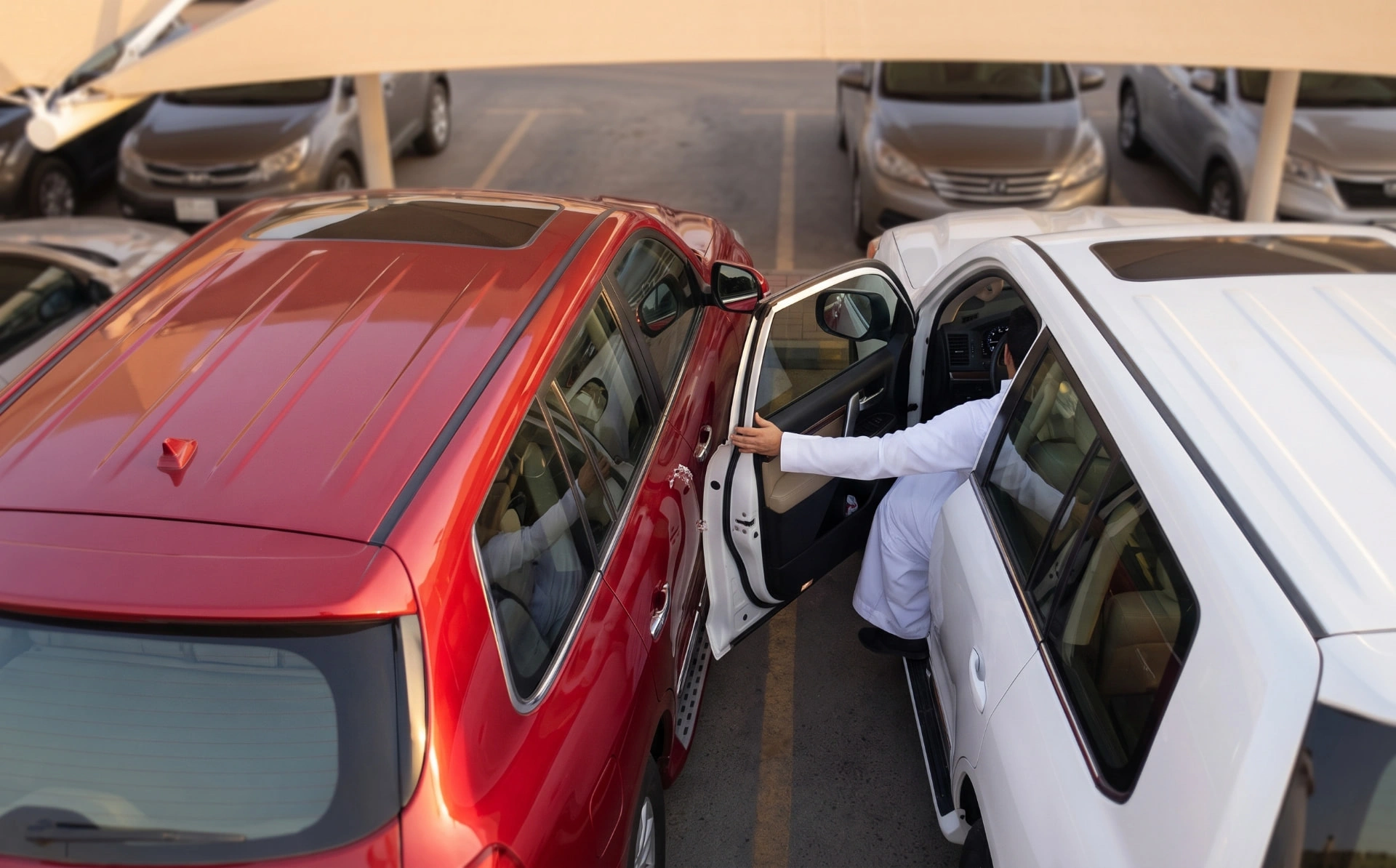 A car door opening into the red SUV parked beside it in a tight parking space